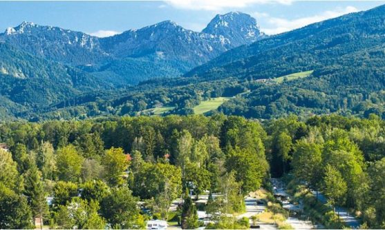 Malerisches Bergpanorama: Blick von oben auf das dicht bewaldete Gelände des Campingplatzes mit dem markanten Bergpanorama der „Schlafenden Jungfrau“ im Hintergrund – Campingplatz Kaiser Camping in Bad Feilnbach.