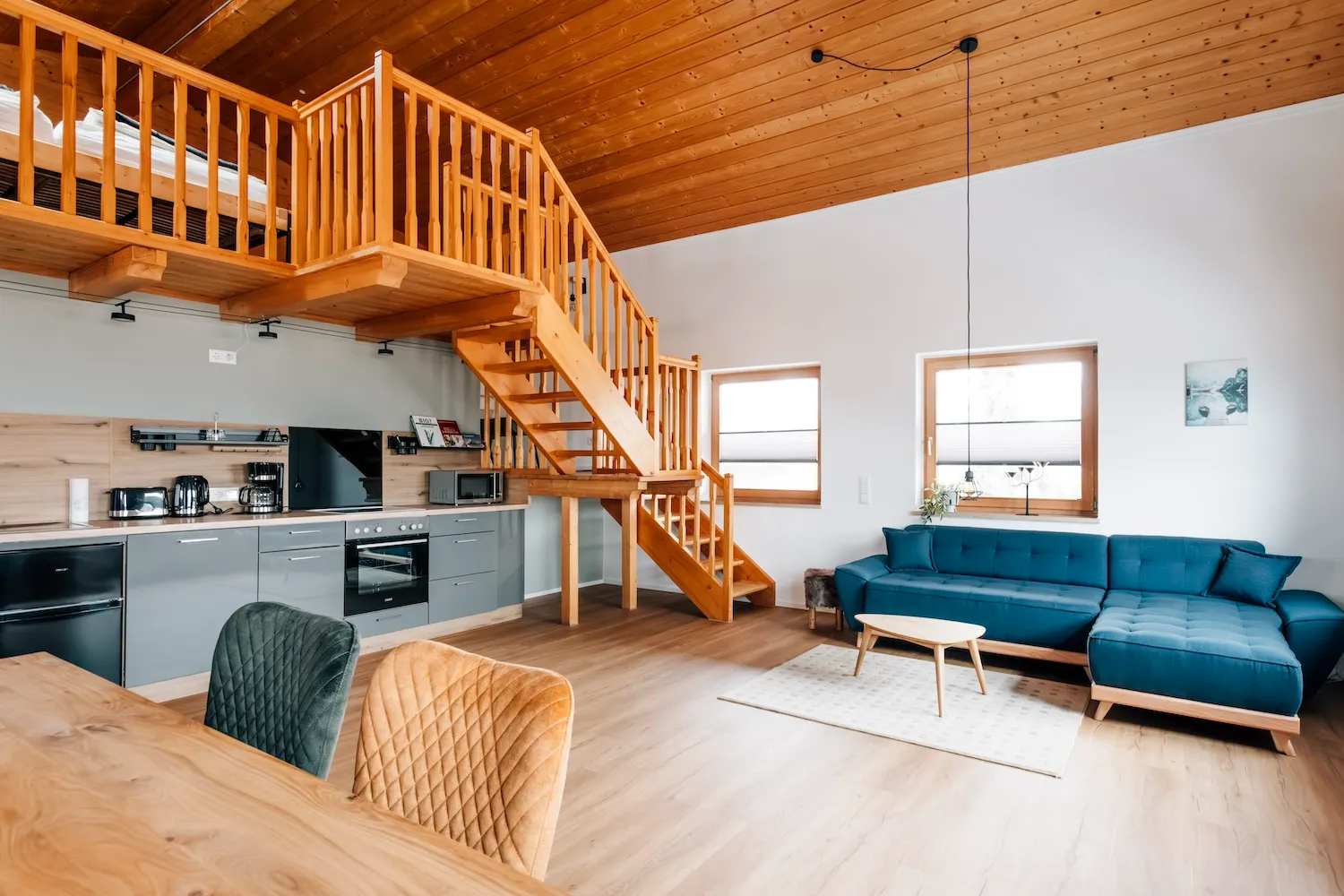 Offener Wohnbereich mit blauem Ecksofa, Holztreppe zur Schlafgalerie und Blick in die Küche – Ferienwohnung Kaiser Franz Josef, Kaiser Camping Bad Feilnbach