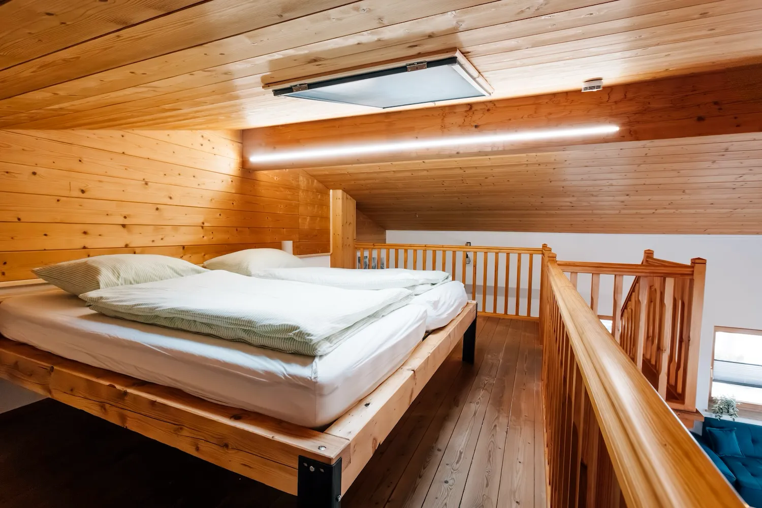 Schlafbereich auf der Holzgalerie der Ferienwohnung Kaiser Franz Josef – Doppelbett unter Dachschräge mit Dachfenster, natürliches Holzambiente - Kaiser Campingplatz in Bad Feilnbach