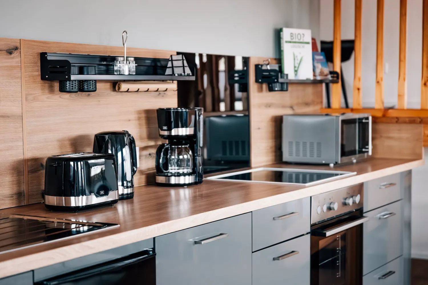 Vollausgestattete Küche der Ferienwohnung Kaiser Franz Josef: Cerankochfeld, Kaffeemaschine, Toaster, Dunstabzug und graue Einbauküche mit Holzarbeitsplatte - Kaiser Campingplatz in Bad Feilnbach