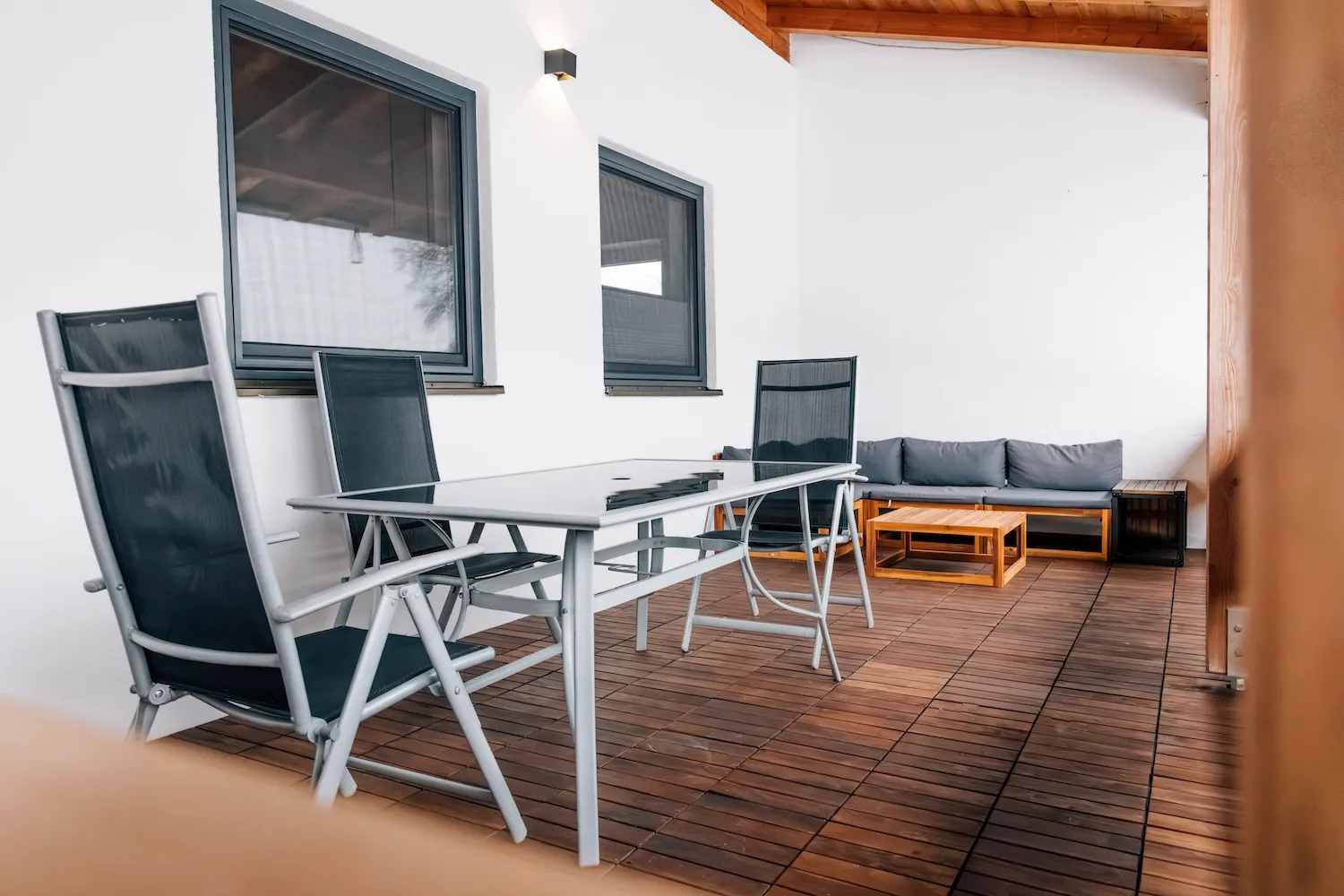 Überdachte Terrasse der Ferienwohnung Kaiser Franz Josef auf dem Kaiser Camping Bad Feilnbach – Sitzgruppe mit Gartenstühlen und Tisch auf Holzdielenboden