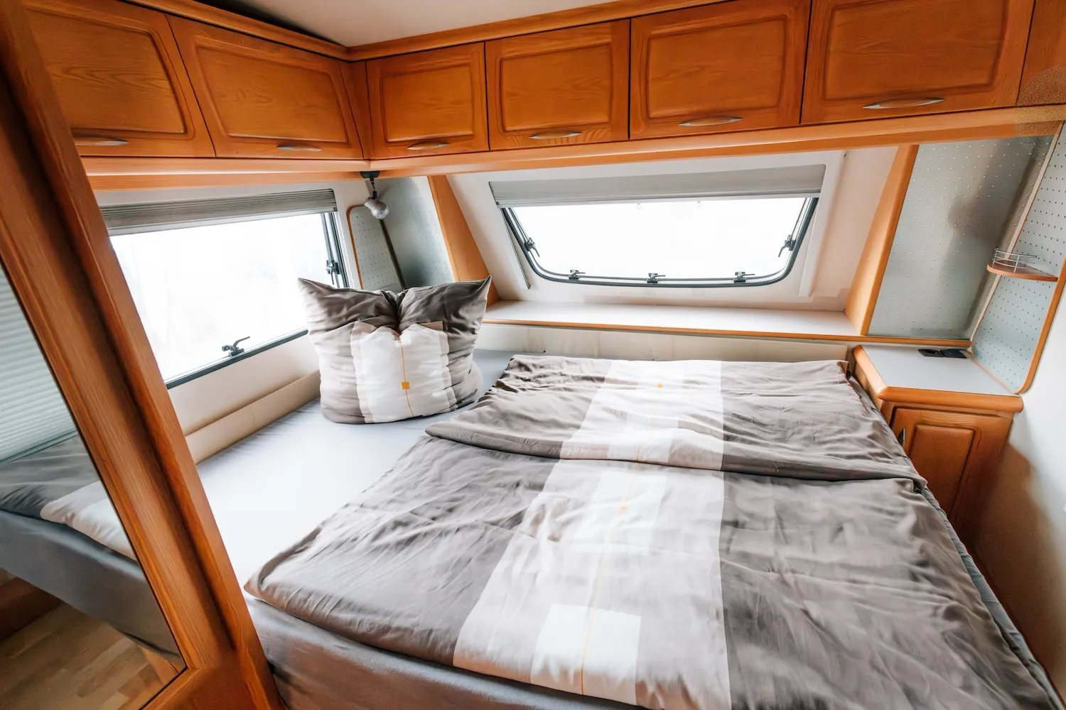 Schlafbereich im Wohnwagen der Camping-Suite Karl Albrecht – Doppelbett unter dem Dach mit Kippfenster und gemütlicher Bettwäsche - Kaiser Campingplatz in Bad Feilnbach