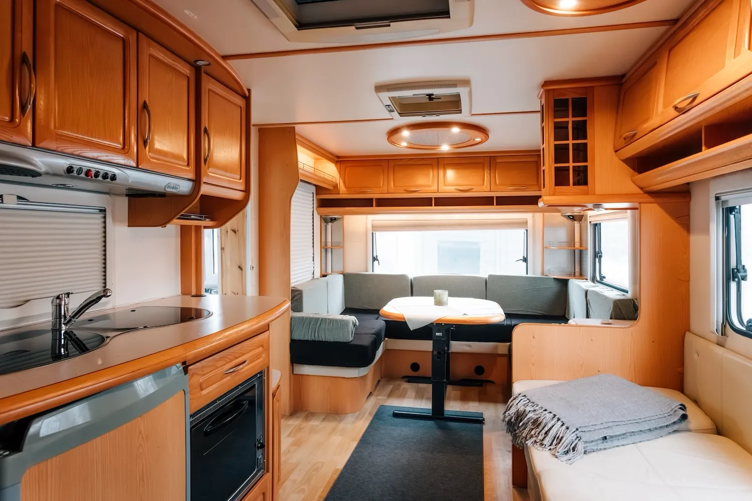 Küchenbereich im Wohnwagen der Camping-Suite Karl Albrecht mit Einbauküche, Kochfeld und Essbereich – typische Wohnwagen-Atmosphäre mit warmem Holzdekor - Kaiser Campingplatz in Bad Feilnbach