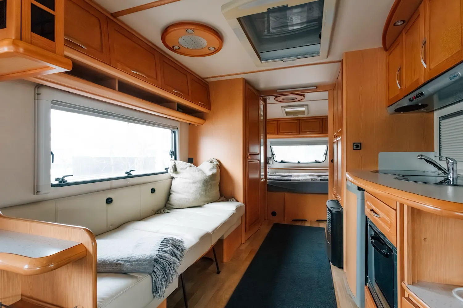 Schlaf- und Küchenbereich im Wohnwagen der Camping-Suite Karl Albrecht – Liegefläche, Einbauküche und Stauraum in klassischer Wohnwagen-Ausstattung - Kaiser Campingplatz in Bad Feilnbach