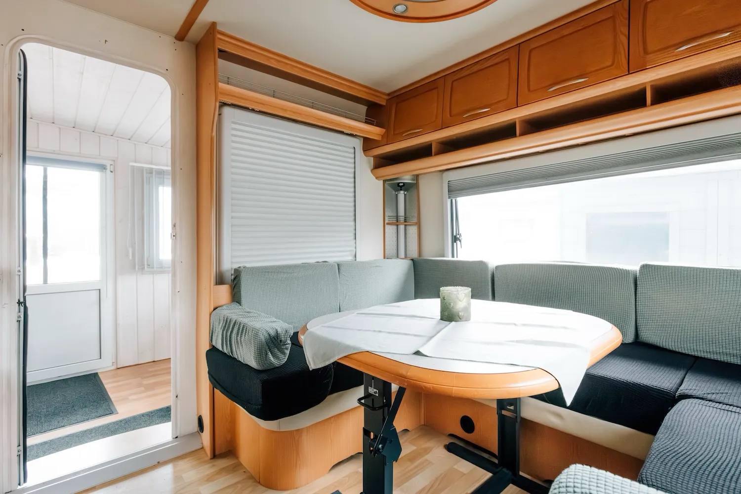 Sitzbereich im Wohnwagen der Camping-Suite Karl Albrecht auf dem Kaiser Camping Bad Feilnbach – Eckbank mit Klapptisch und Staufächern über den Fenstern - Kaiser Campingplatz in Bad Feilnbach