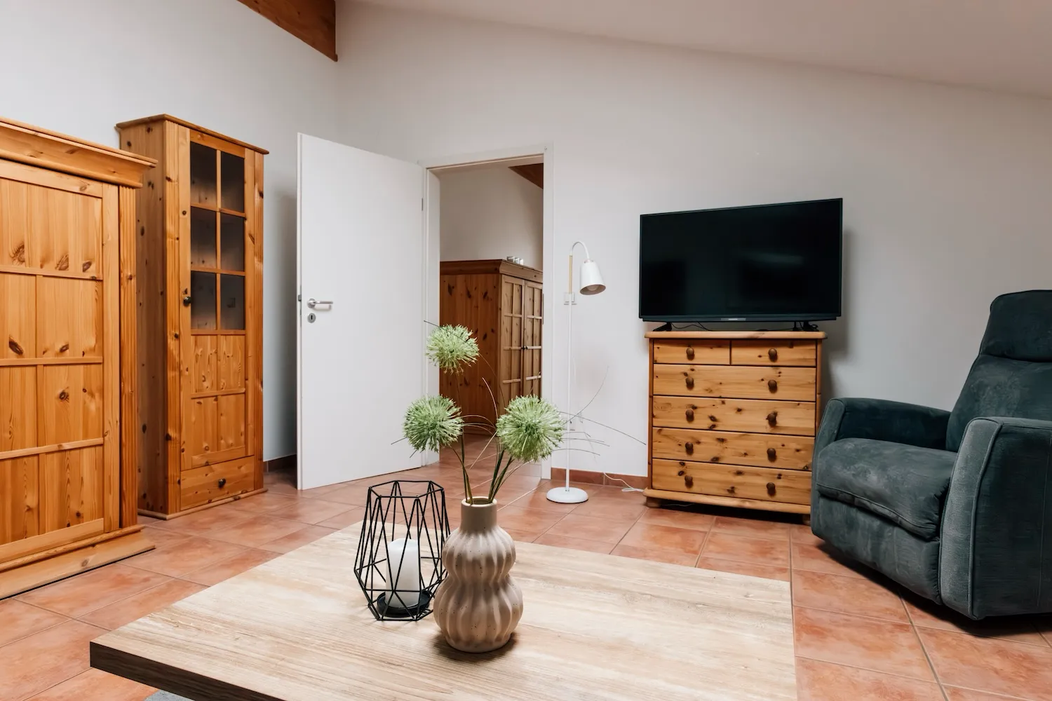 Wohnbereich der Ferienwohnung König Ludwig: Massivholzschrank in Kiefernoptik, Flachbild-TV und Relaxsessel auf hellem Parkettboden - Kaiser Campingplatz in Bad Feilnbach