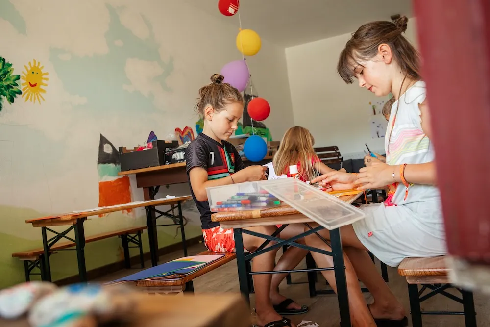 Zwei Kinder konzentrieren sich beim Basteln am Tisch, begleitet von ihren Animateuren im Kids-Club, Teil des bunten Ferienprogramms auf dem Campingplatz Kaiser Camping in Bad Feilnbach.
